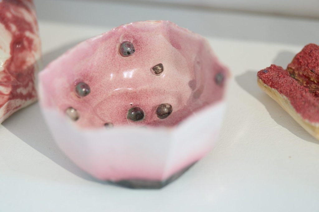 A small ceramic bowl with angular sides. The inside is blush pink with small green lumps across the otherwise smooth surface.